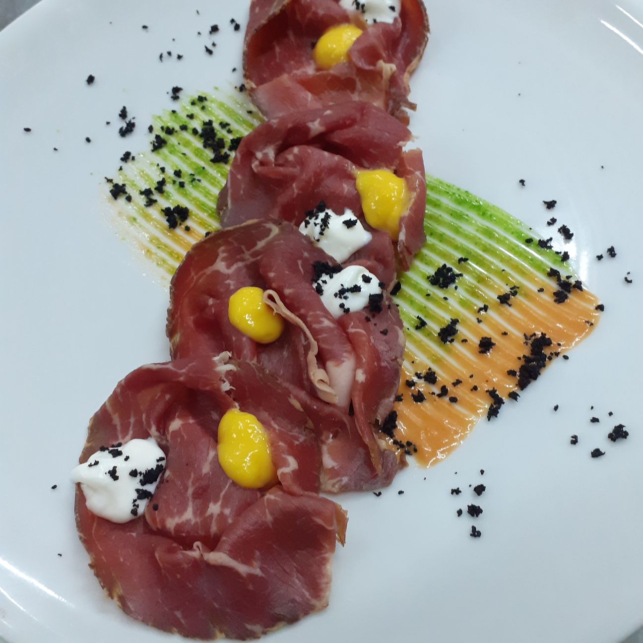 Carpaccio di Black Angus affumicato su salsa di Rucola e pomodorino confit con salsa di peperone giallo maturato in Agrodolce ,Mousse di Burrata di Andria e Polvere di olive