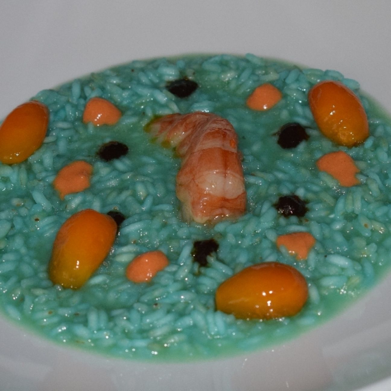 Risotto al curacao blu con gamberi, crema all'aglio nero e kumquat caramellati.