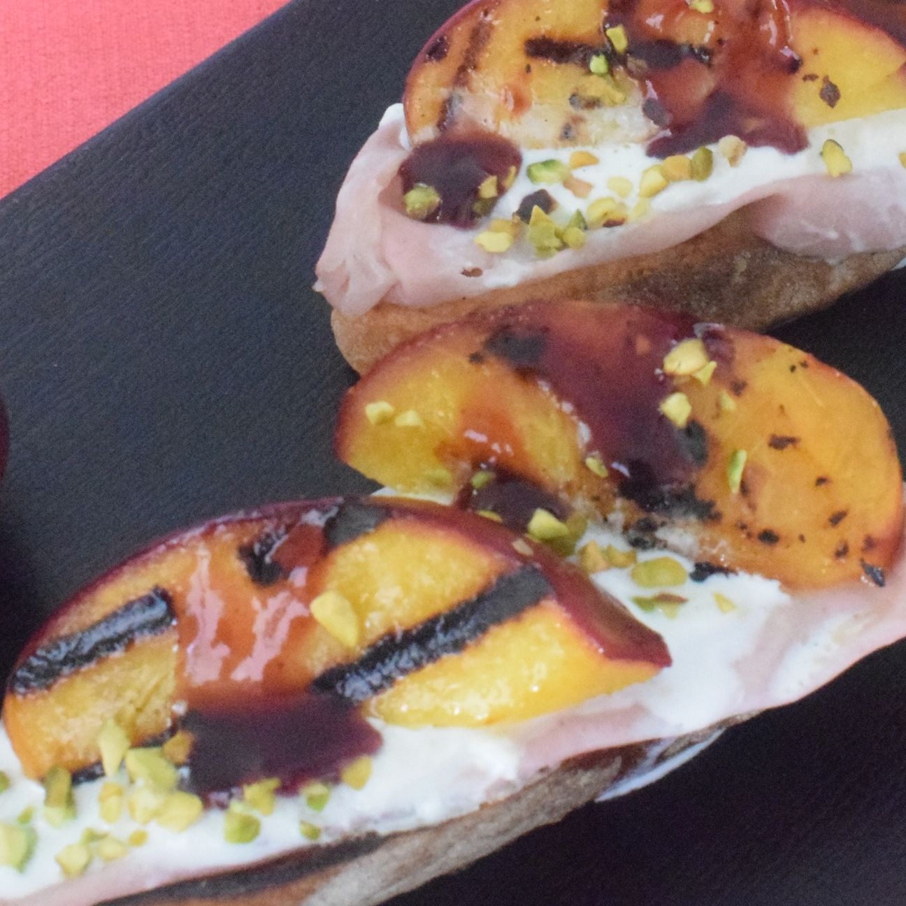 Bruschette con pesche grigliate, stracciatella e riduzione di vino.