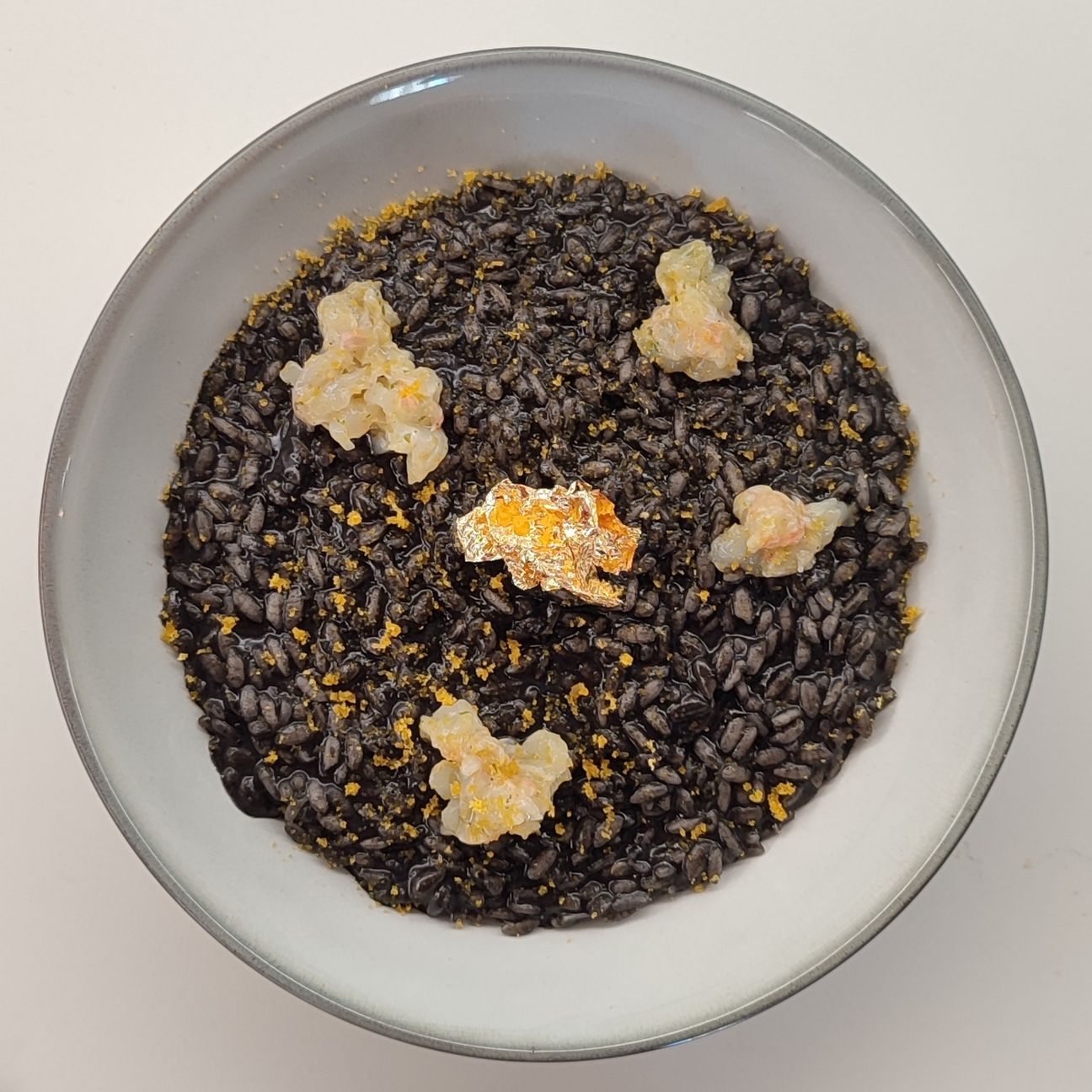 Risotto al nero di seppia con tartare di scampi, bottarga e foglia d'oro