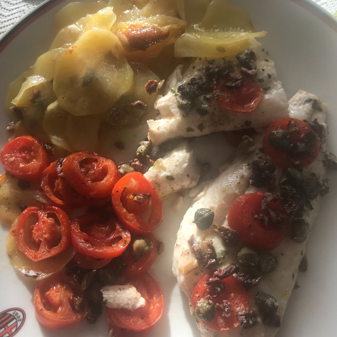 Filetti di nasello al forno su un letto di patata pomodorini olive taggiasche e capperi