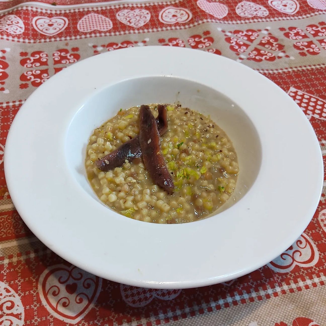 Fregola con filetti di acciughe, vino bianco Pecorino, scorza di limone e pepe nero.