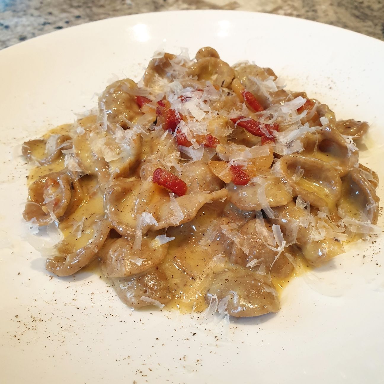 Orecchiette di grano arso con crema di tuorlo e grana, guanciale di maialino nero, pepi tostati e fiocchi di pecorino toscano