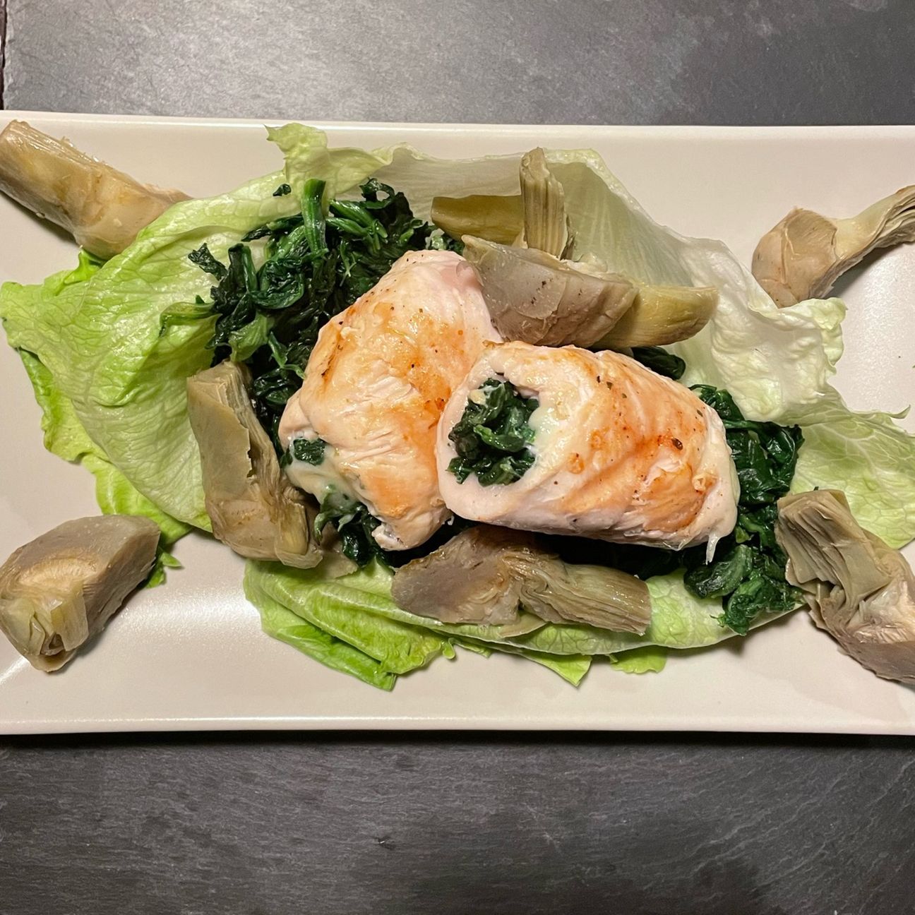 Involtini di petto di pollo con spinaci e scamorza, serviti con spinaci, carciofi e una foglia di insalata iceberg