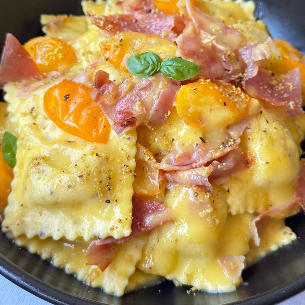 Ravioli cacio e pepe Fini Modena con datterini gialli e speck