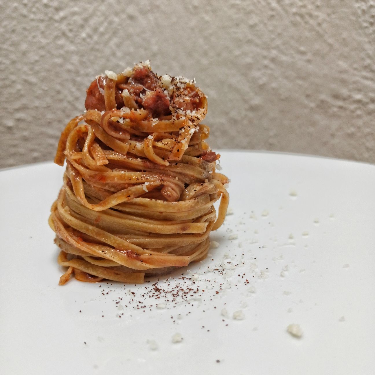 Tagliolini all'uovo, con crema di pomodori secchi, pancetta steccata, pecorino, polvere di melanzana.