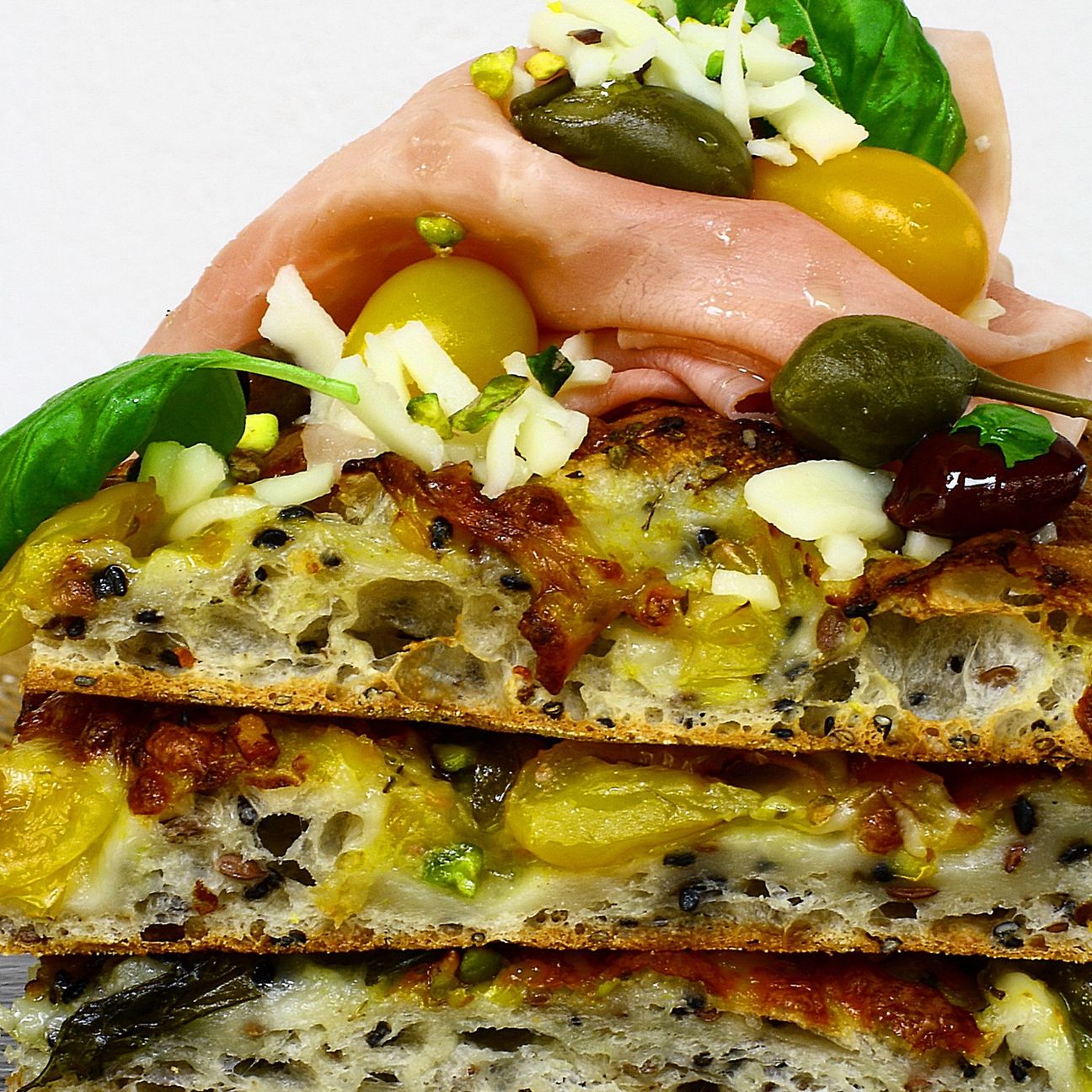 Pizza in pala ai semi di lino e sesamo, mozzarella, taggiasche, capperi e cotto in uscita