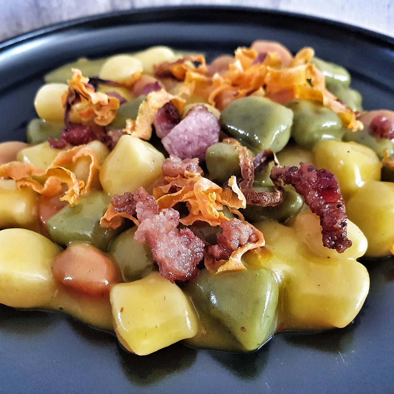 Chicche tricolore con besciamella allo zafferano, bacon e chips di carote