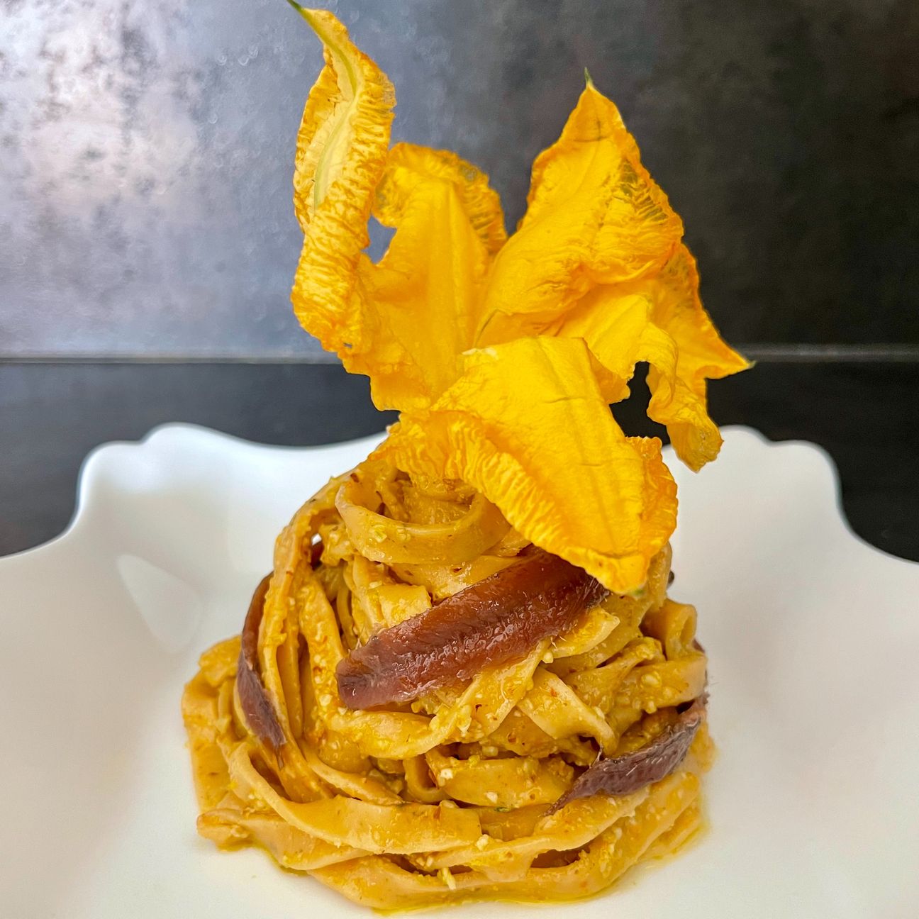 Tagliatelle al pomodoro piccante con pesto di fiori di zucca e filetti di acciughe